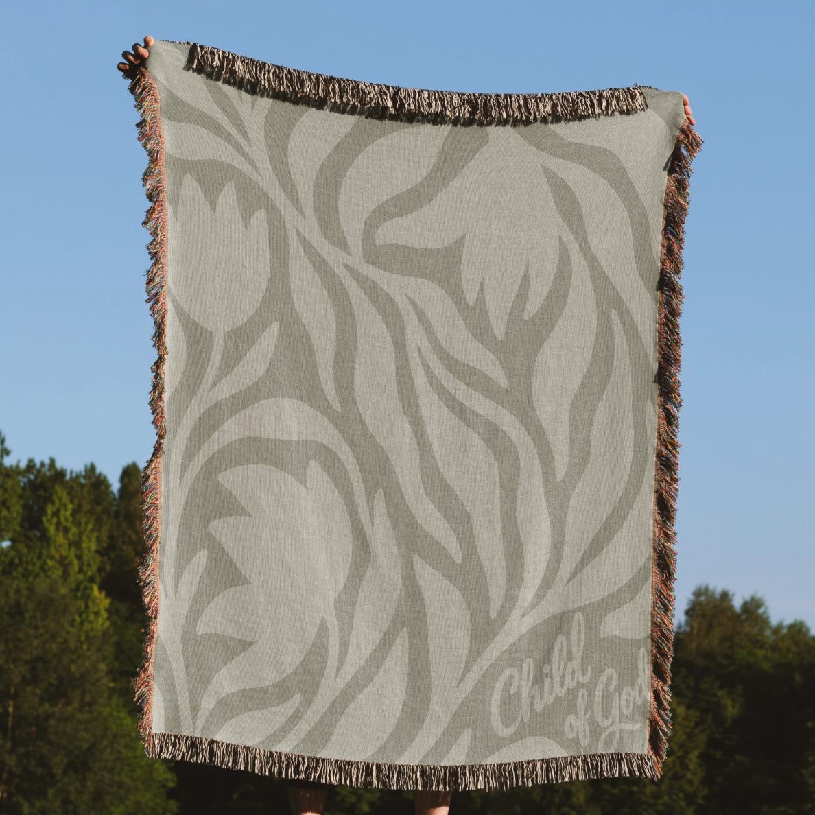 Green earthy-toned woven blanket with foliage pattern and “Child of God” text; made of 100% cotton with fringe, ideal for nurseries, kids’ rooms, or Christian gifts.