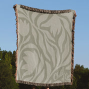 Green earthy-toned woven blanket with foliage pattern and “Child of God” text; made of 100% cotton with fringe, ideal for nurseries, kids’ rooms, or Christian gifts.