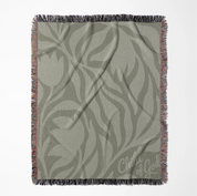 Green earthy-toned woven blanket with foliage pattern and “Child of God” text; made of 100% cotton with fringe, ideal for nurseries, kids’ rooms, or Christian gifts.