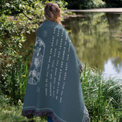 Person wrapped in a blue prayer blanket by a pond