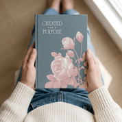 Woman in cozy sweater holding Created for a Purpose christian journal showing front cover