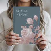 Person holding a book titled 'Created for a Purpose' with floral design