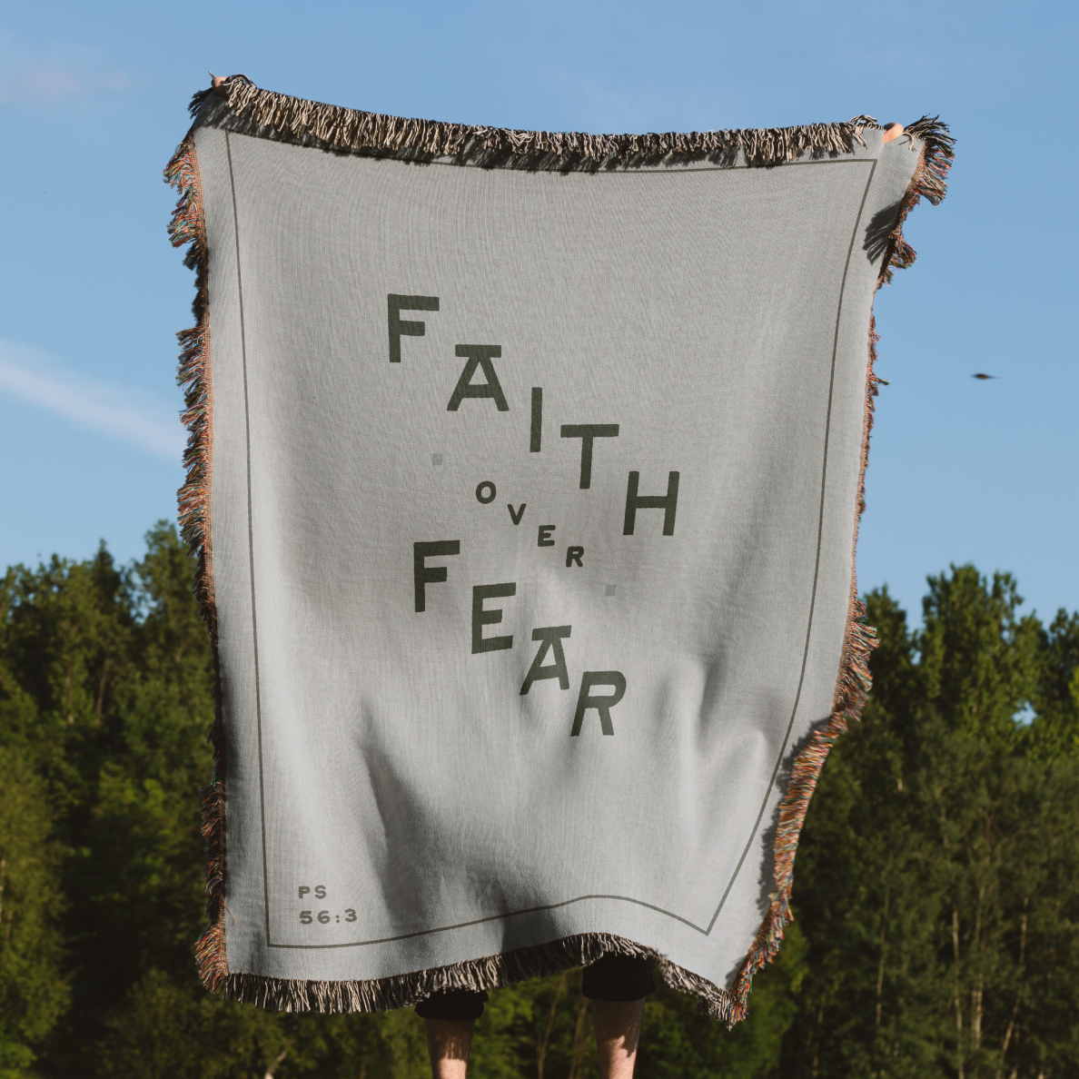 Gray blanket with 'Faith Over Fear' text held by a person outdoors