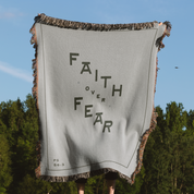 Gray blanket with 'Faith Over Fear' text held by a person outdoors