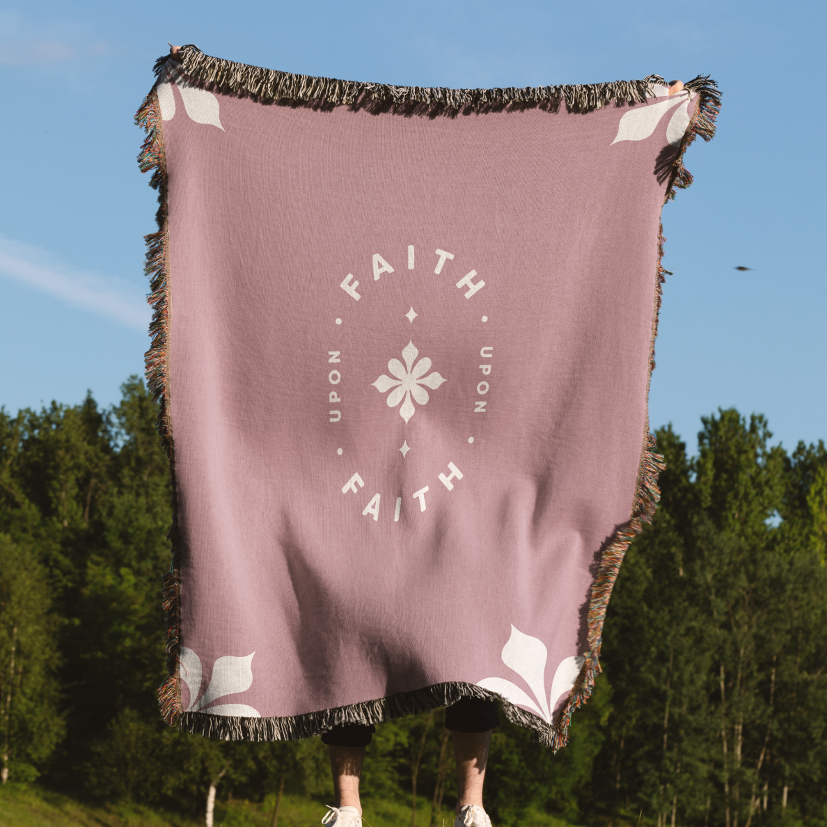 Person holding a purple blanket with 'Faith Upon Faith' text and floral design against a natural background.