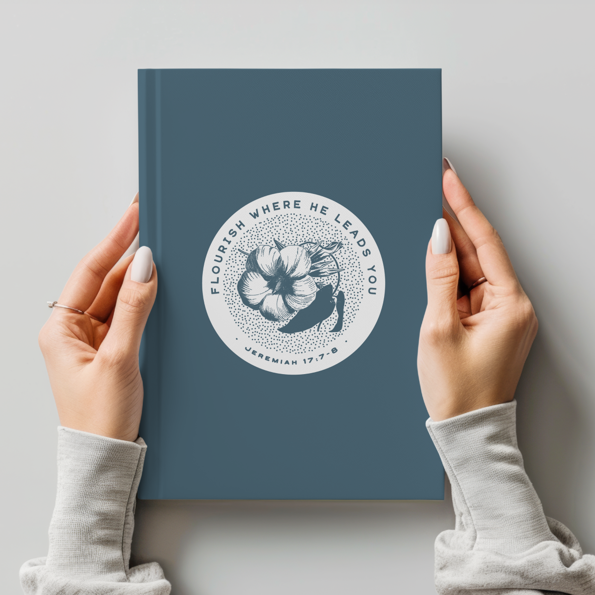 Blue notebook with floral design and text held by hands against a light gray background