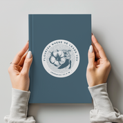 Blue notebook with floral design and text held by hands against a light gray background