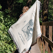 Person holding a large decorative blanket with fruit design and text in a forest setting