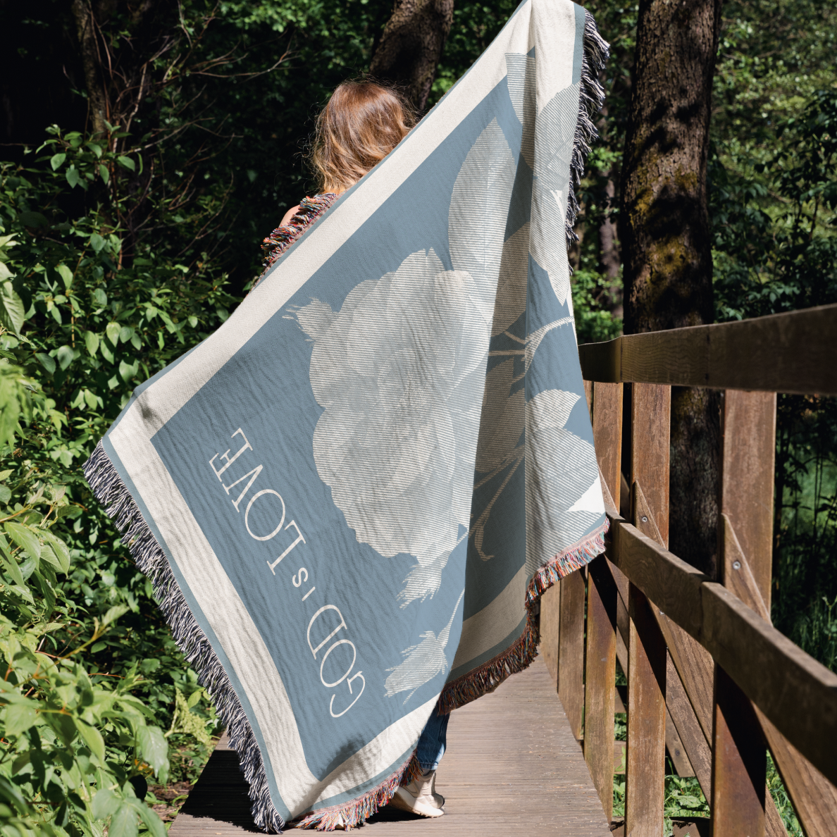 Person holding a decorative blanket with floral design and 'LOVE' text in a forest setting