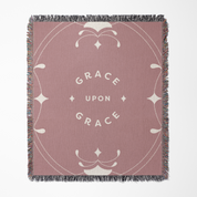 Pink blanket with 'Grace Upon Grace' text and decorative elements on a white background