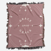 Pink throw blanket with 'Grace Upon Grace' text and decorative patterns on a white background