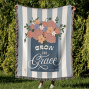 Striped blanket with floral design and 'Grow in Grace' text held by a person outdoors.