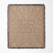 Neutral-toned woven blanket with the phrase "Grow in Grace" surrounded by elegant floral design; made from 100% cotton with fringe, perfect Christian gift or decor.