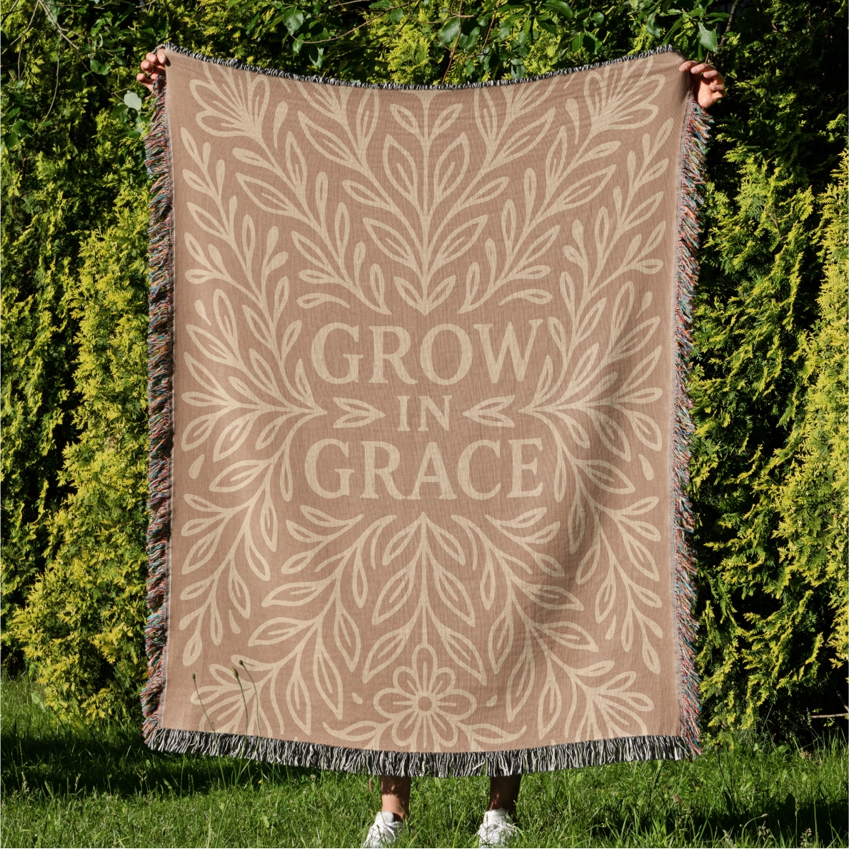 Neutral-toned woven blanket with the phrase "Grow in Grace" surrounded by elegant floral design; made from 100% cotton with fringe, perfect Christian gift or decor.