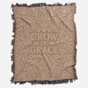 Neutral-toned woven blanket with the phrase "Grow in Grace" surrounded by elegant floral design; made from 100% cotton with fringe, perfect Christian gift or decor.