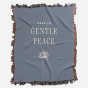 Blue blanket with 'Held in Gentle Peace' text and a dandelion graphic on a white background