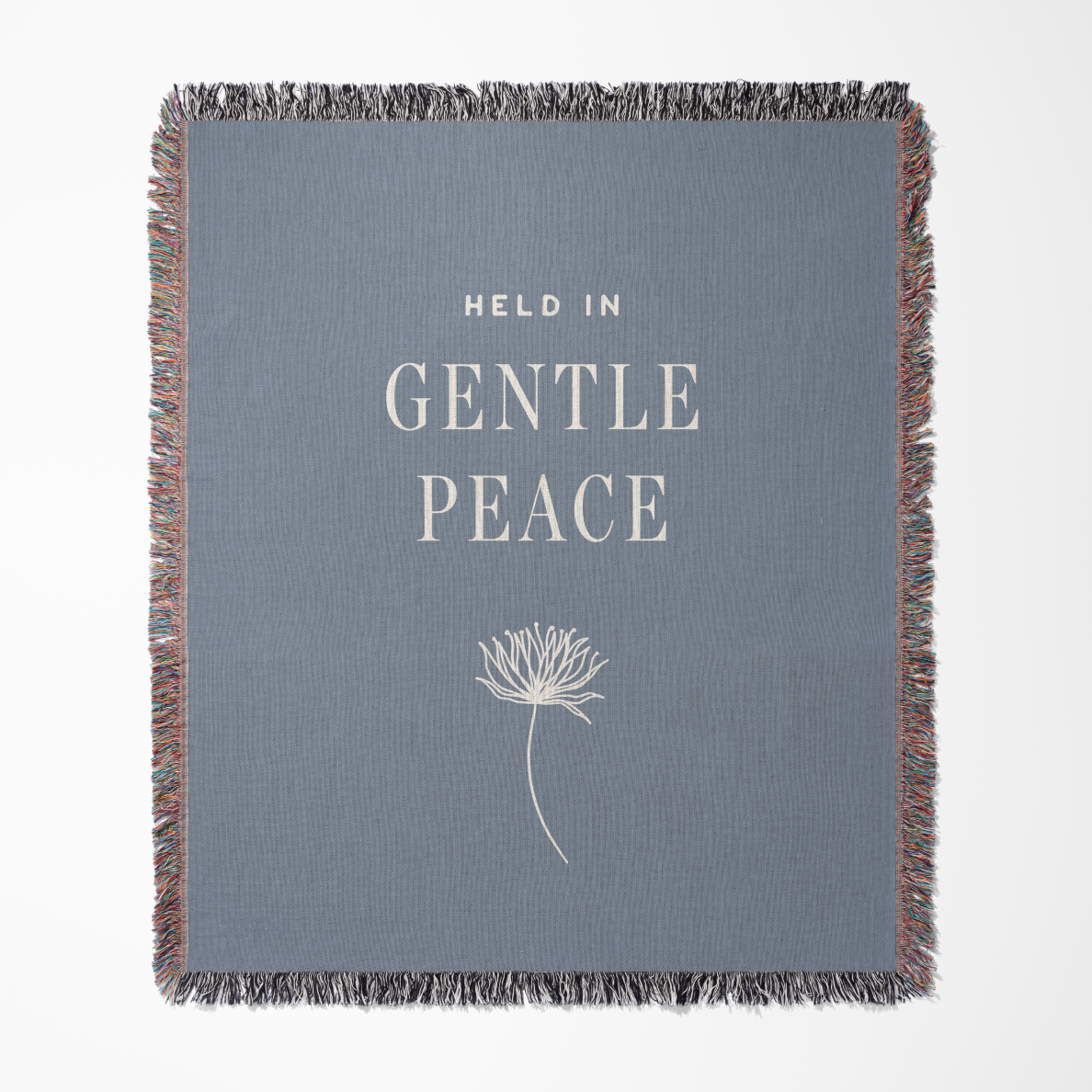 Gray blanket with 'Held in Gentle Peace' text and dandelion graphic on a white background