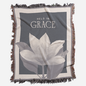 Blanket with floral design and 'Held in Grace' text on a gray background