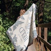 Person holding a patterned blanket with text and graphics in a forest setting