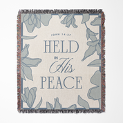 Blanket with floral design and text 'HELD IN HIS PEACE' and 'John 14:27' on a white background