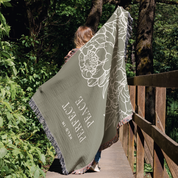 Person holding a green blanket with floral design and text in a forest setting