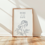 Framed artwork with floral design and 'HERE YOU ARE SAFE' text on a wall.