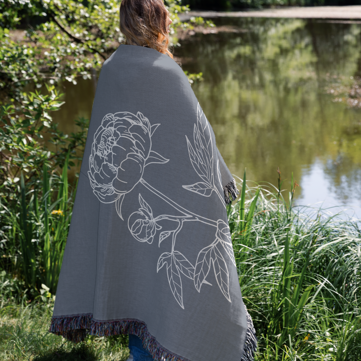 Person wearing a gray blanket with floral design by a pond