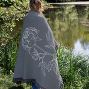 Person wearing a gray blanket with floral design by a pond