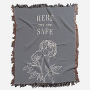 Gray blanket with floral design and 'Here You Are Safe' text on a white background