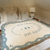 Blanket with 'His Grace Sustains Me' text on a bed in a bedroom setting