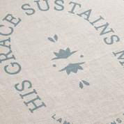 Textured fabric with 'His Grace Sustains My Land' printed in blue on a beige background