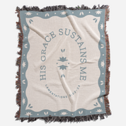 Blanket with 'His Grace Sustains Me' text and decorative border on a white background