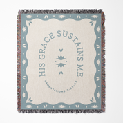 Blanket with 'His Grace Sustains Me' text and decorative border on a white background