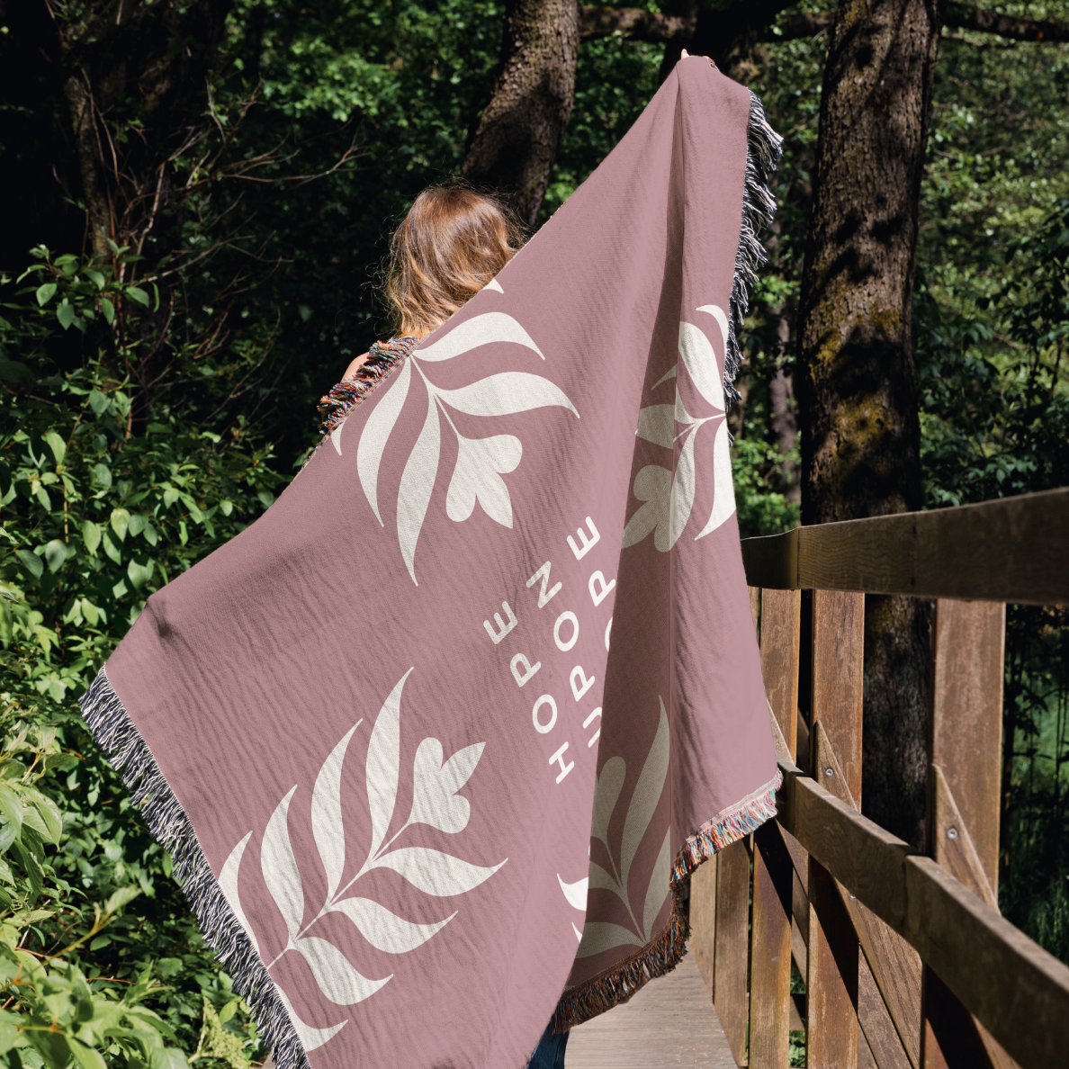 Person holding a pink blanket with leaf patterns and 'Hope' text in a forest setting
