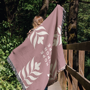 Person holding a pink blanket with leaf patterns and 'Hope' text in a forest setting