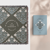 Decorative blanket with floral pattern and motivational quote, next to a matching notebook on a neutral background.
