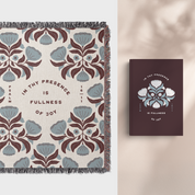 Decorative blanket with floral pattern and text, matching a book titled 'In Thy Presence is Fullness of Joy' on a neutral background.