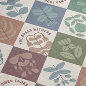 Patterned fabric with leaf designs and 'The Grass Withers' text on a checkered background.