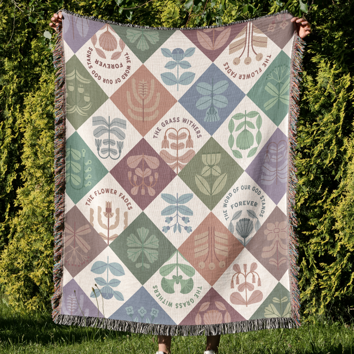 Patterned blanket held up outdoors with greenery in the background