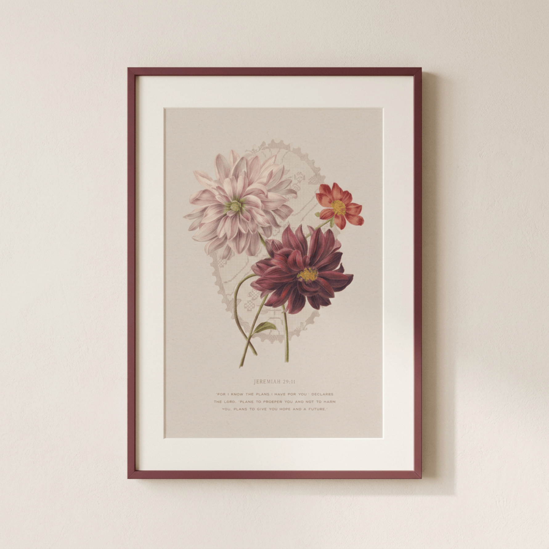 A framed botanical art print featuring three dahlia flowers in soft pink, burgundy, and orange tones on a warm beige background, hung on a light beige wall.