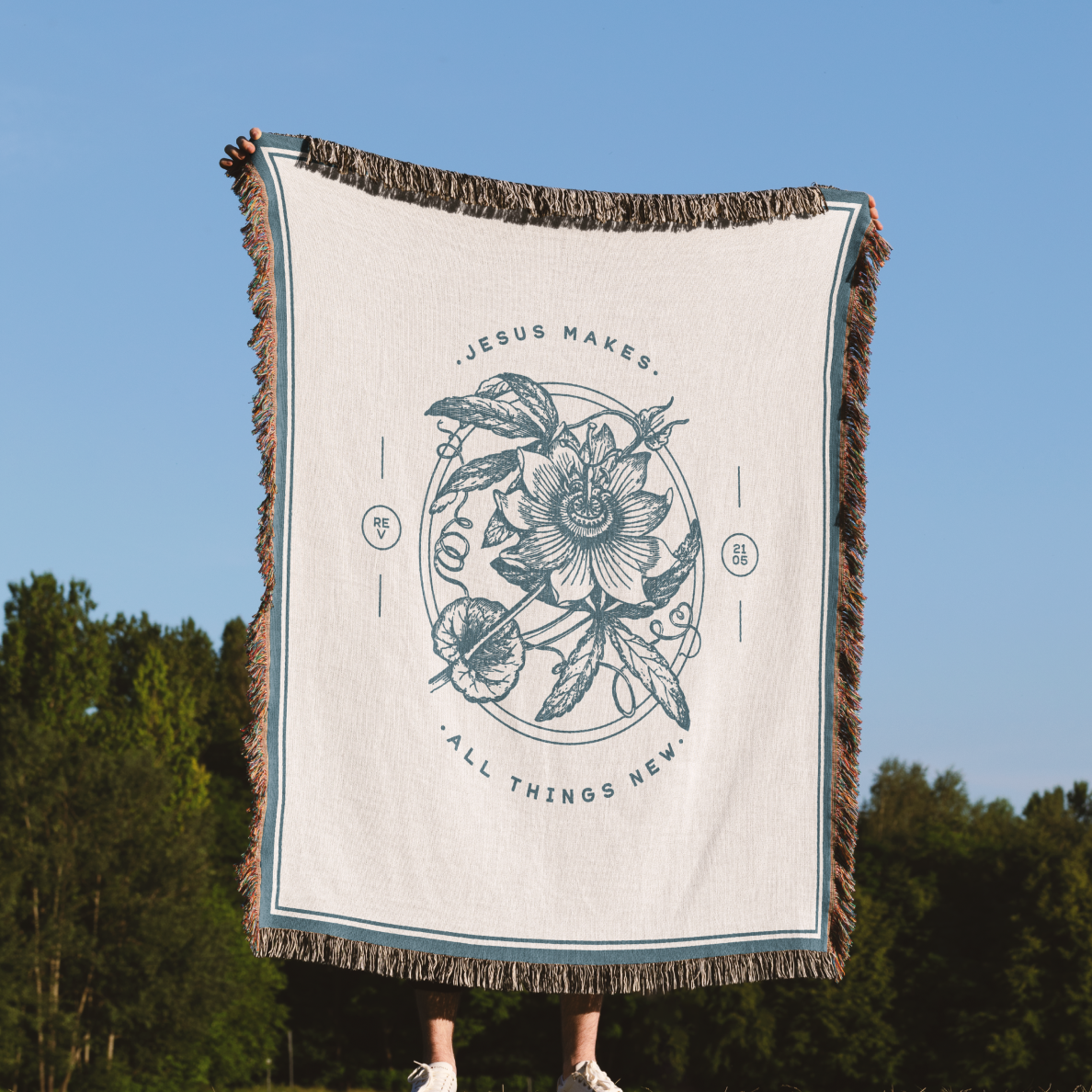 Person holding a blanket with floral design and text against a blue sky and green trees background