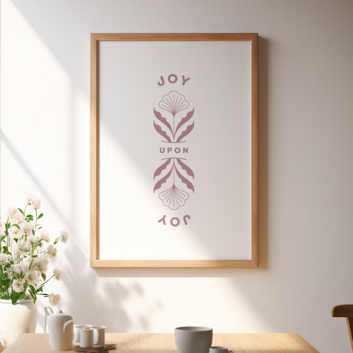 Framed artwork with 'JOY' text and floral design on a wall above a table with decor items.