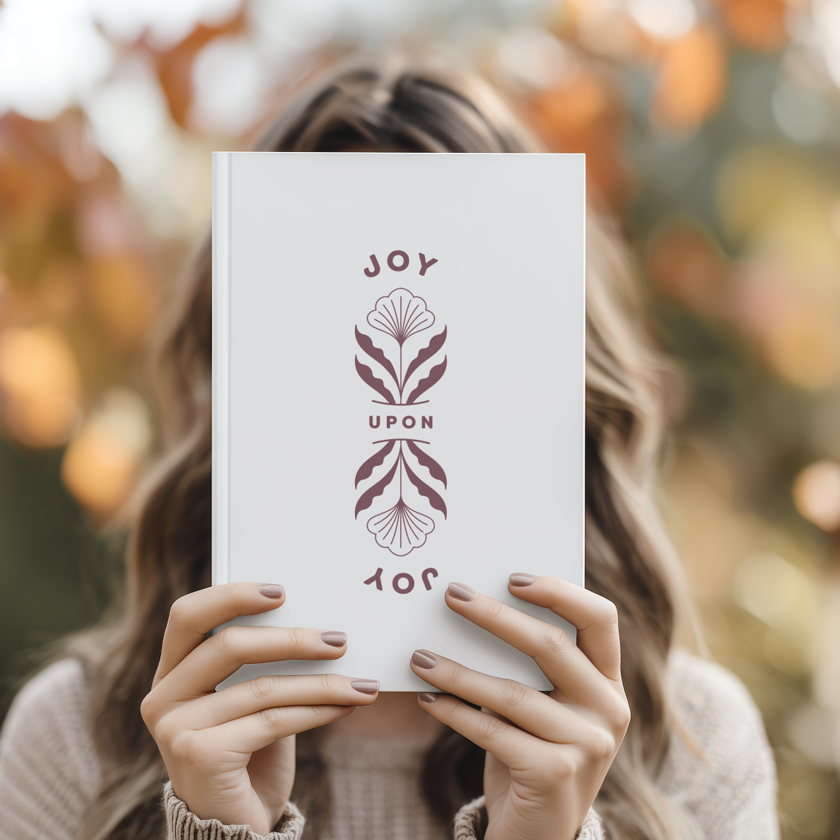 Person holding a book titled 'Joy Upon You' with a blurred autumn background