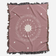 Pink throw blanket with 'Light Upon Light' design and fringed edges on a white background