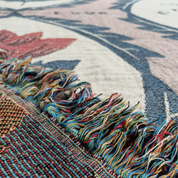 Close-up of a woven rug with multicolored fringe and a floral pattern in cream, dusty pink, blue-gray, and rust red.