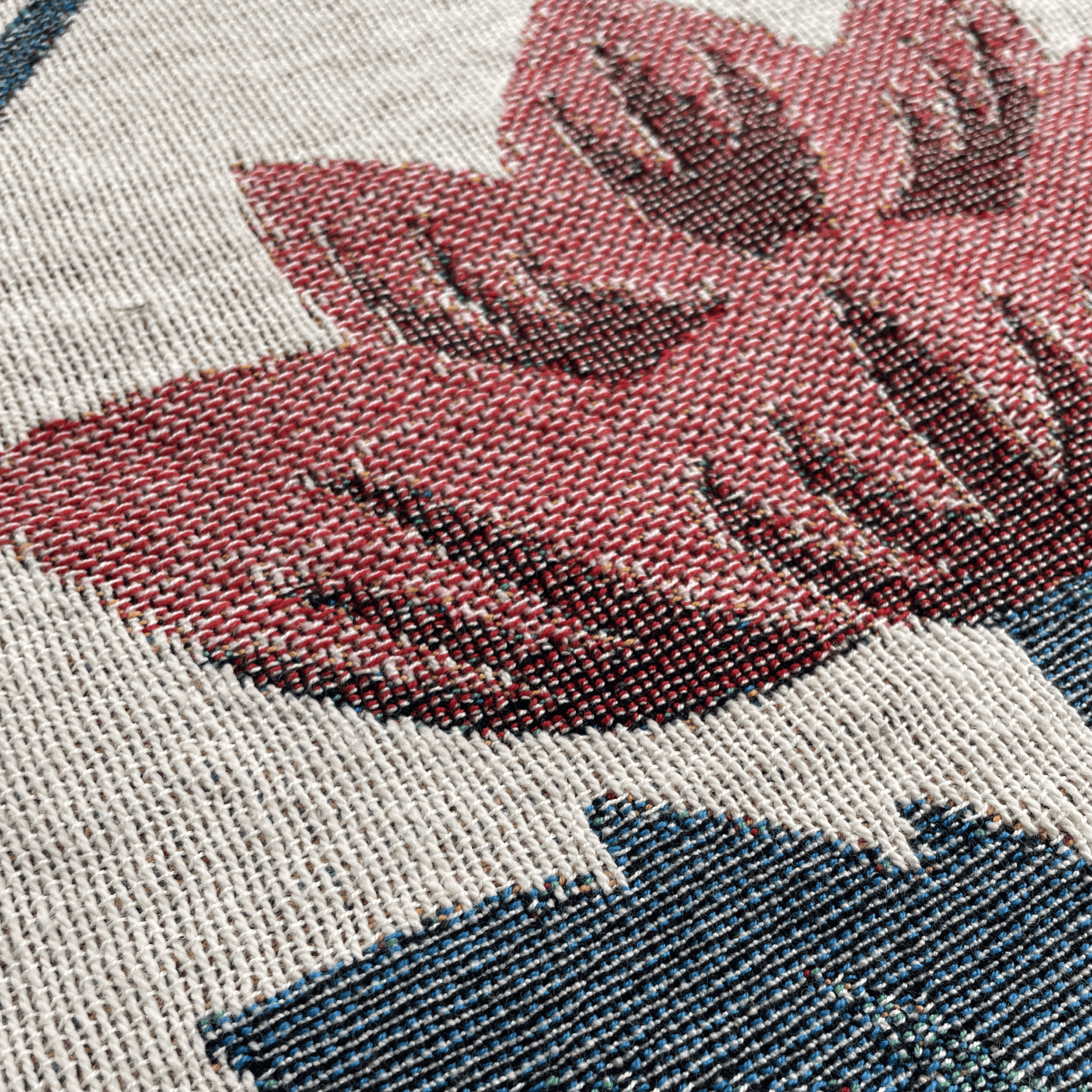 Close-up of a woven textile pattern showing a large muted red leaf motif over a light beige background with a dark blue section below.