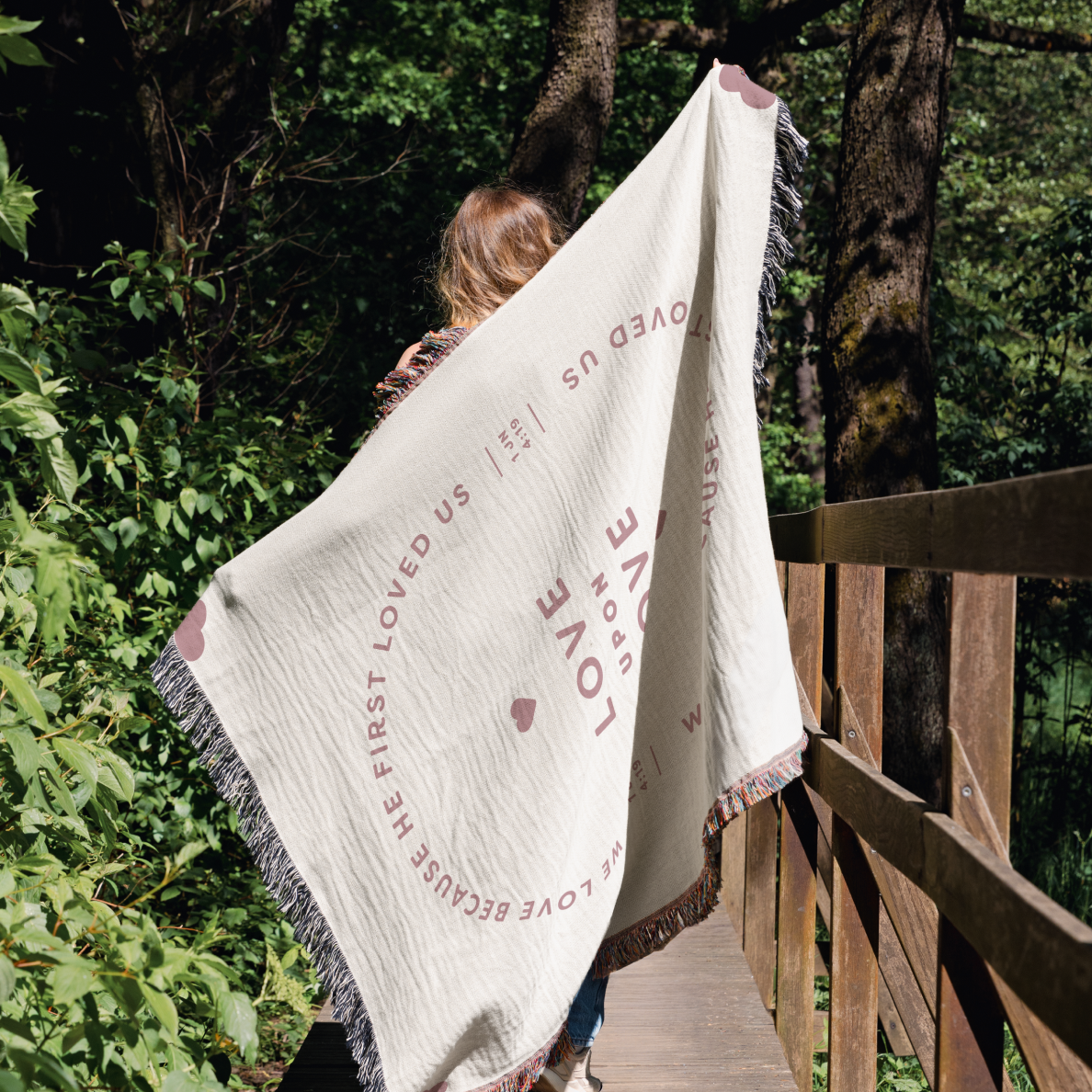 Person holding a white blanket with text and heart design in a forest setting
