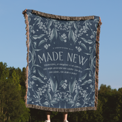 Floral patterned blanket with 'Made New' text against a blue sky and trees background