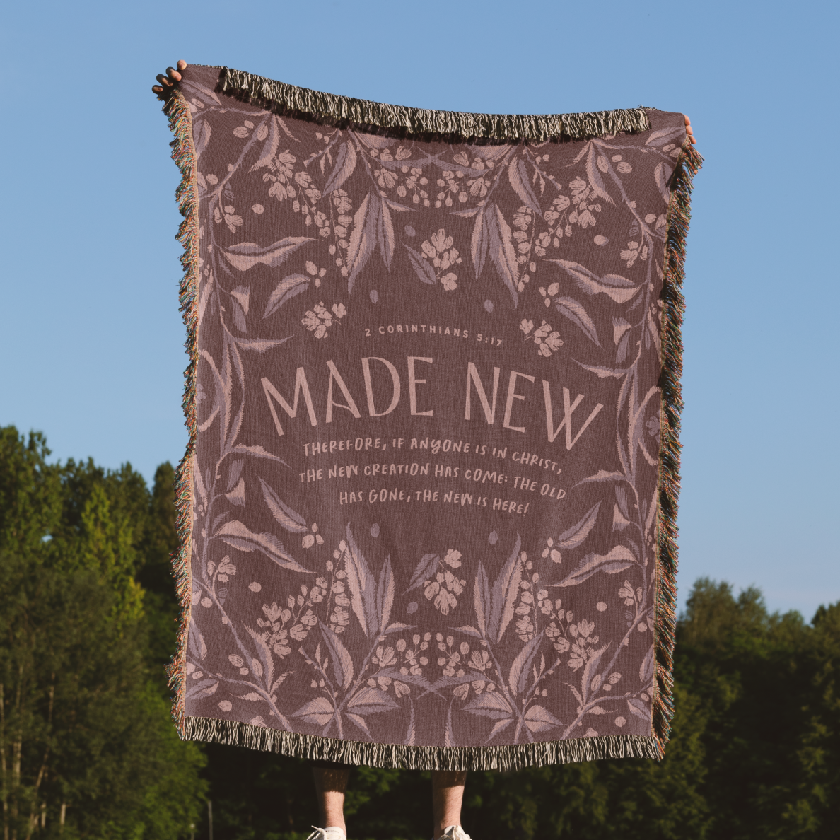 Floral patterned blanket with text against a blue sky and green trees background