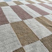 A close-up of a woven textile with a large checkered pattern in muted dusty pink, tan, brown, and off-white.